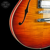 Close-up of a double-cutaway electric guitar body showing a vibrant sunburst finish that transitions from bright orange to deep brown, with a black f-hole and chrome hardware, set against a solid black background.