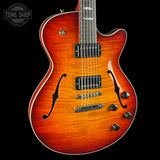 A close-up of a double-cutaway electric guitar with a vibrant sunburst finish, featuring a flamed maple top, black f-holes, dual humbucker pickups, and chrome hardware, set against a solid black background.