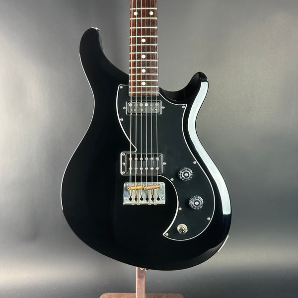 Black electric guitar on a stand against a gray background