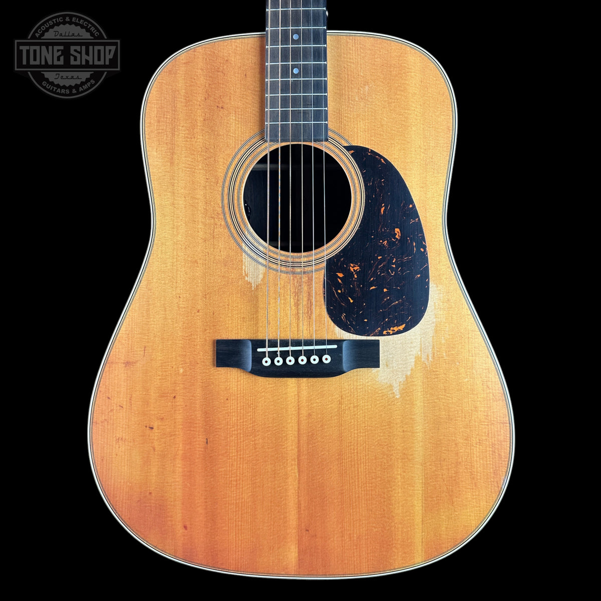 A vintage-style acoustic guitar with a natural sunburst finish, black pickguard, and black bridge, shown against a solid black background with a Tone Shop watermark in the top left corner.