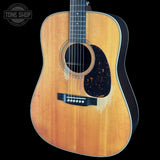 A classic acoustic guitar with a natural wood finish and a black pickguard, shown against a solid black background with a Tone Shop watermark in the top left corner.