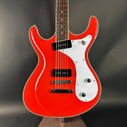 Red electric guitar with white pickguard on a dark background
