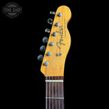 Close-up of the headstock of a Fender Custom Stratocaster electric guitar against a solid black background, showing the maple wood headstock, six silver tuning pegs, and the Fender logo.