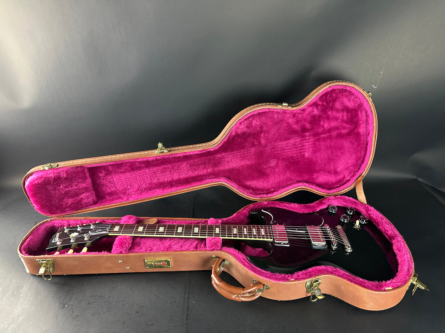 Guitar in an open case with pink interior on a dark background