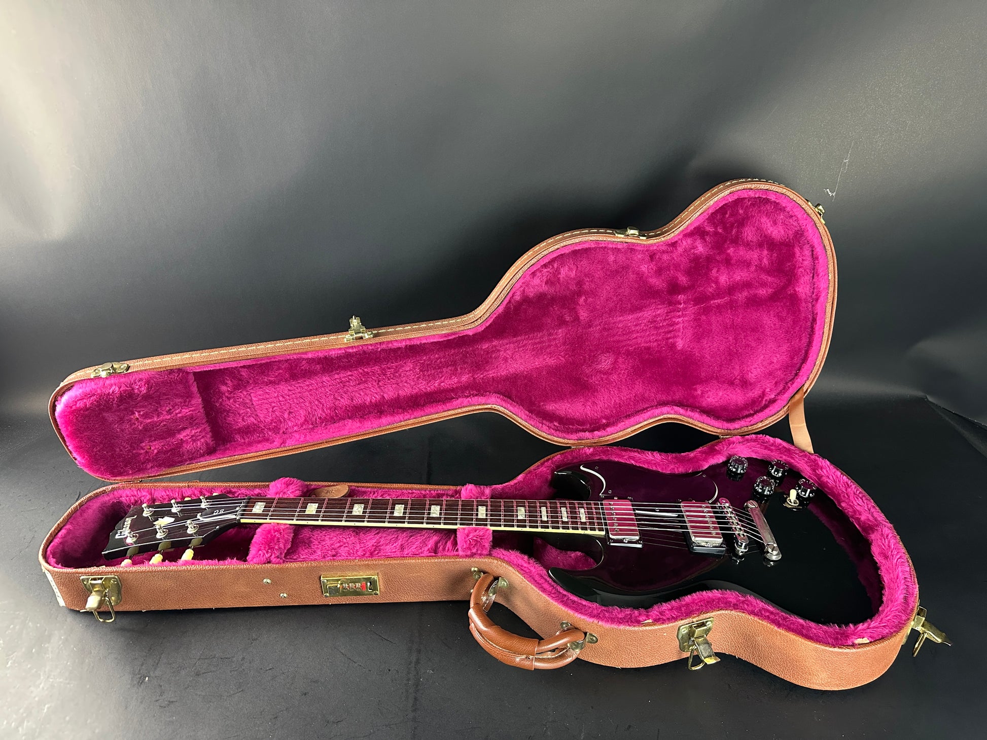 Guitar in an open case with pink interior on a dark background