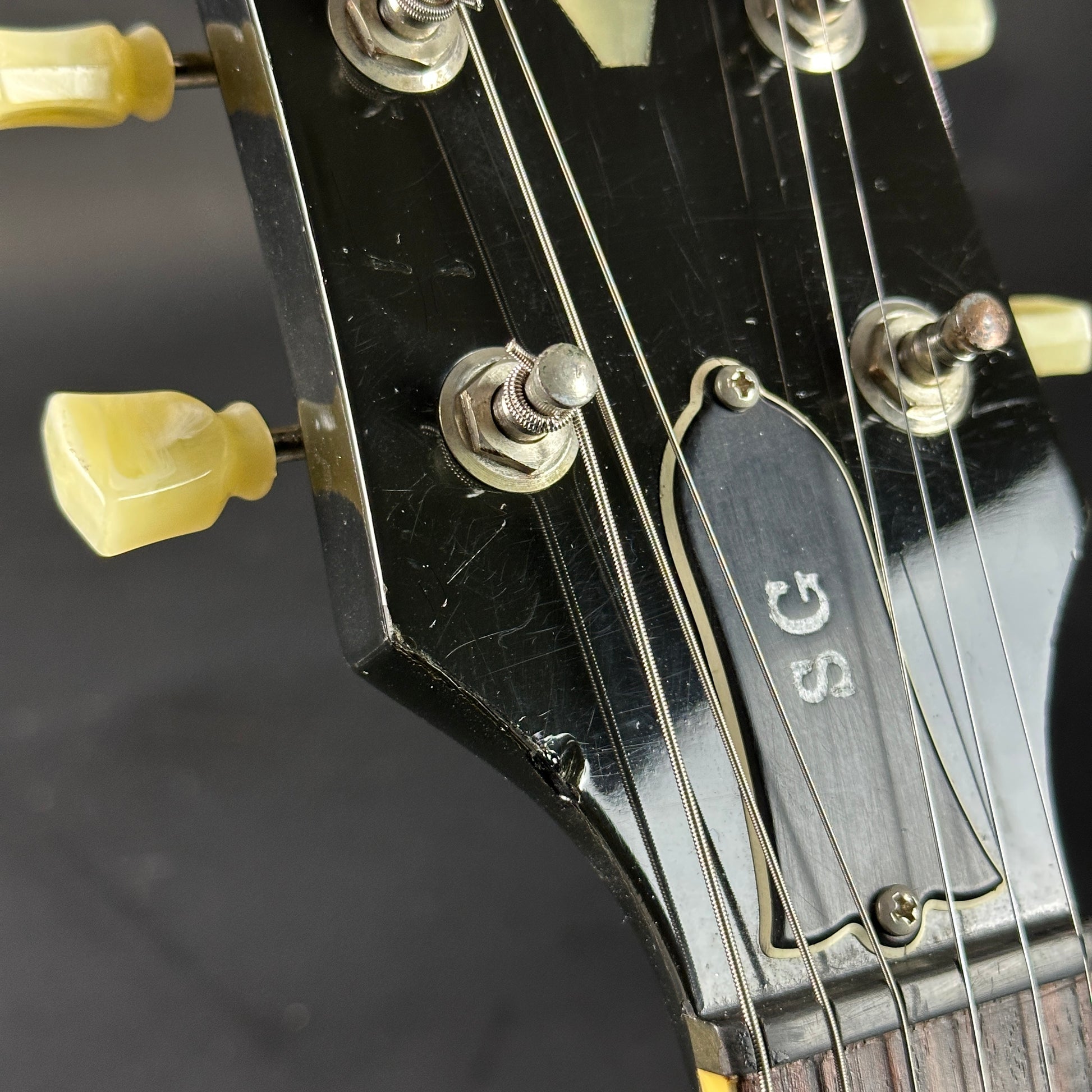 Close-up of a guitar headstock with 'SG' branding on a dark background