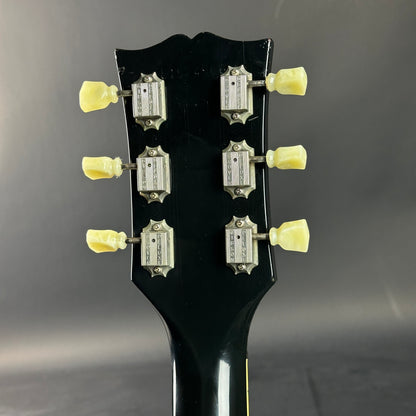 Close-up of a guitar headstock with tuning pegs on a dark background