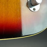 Close-up detail of a sunburst electric guitar body showing the wood grain transition from orange to red to black, with a chrome control knob and binding edge visible.