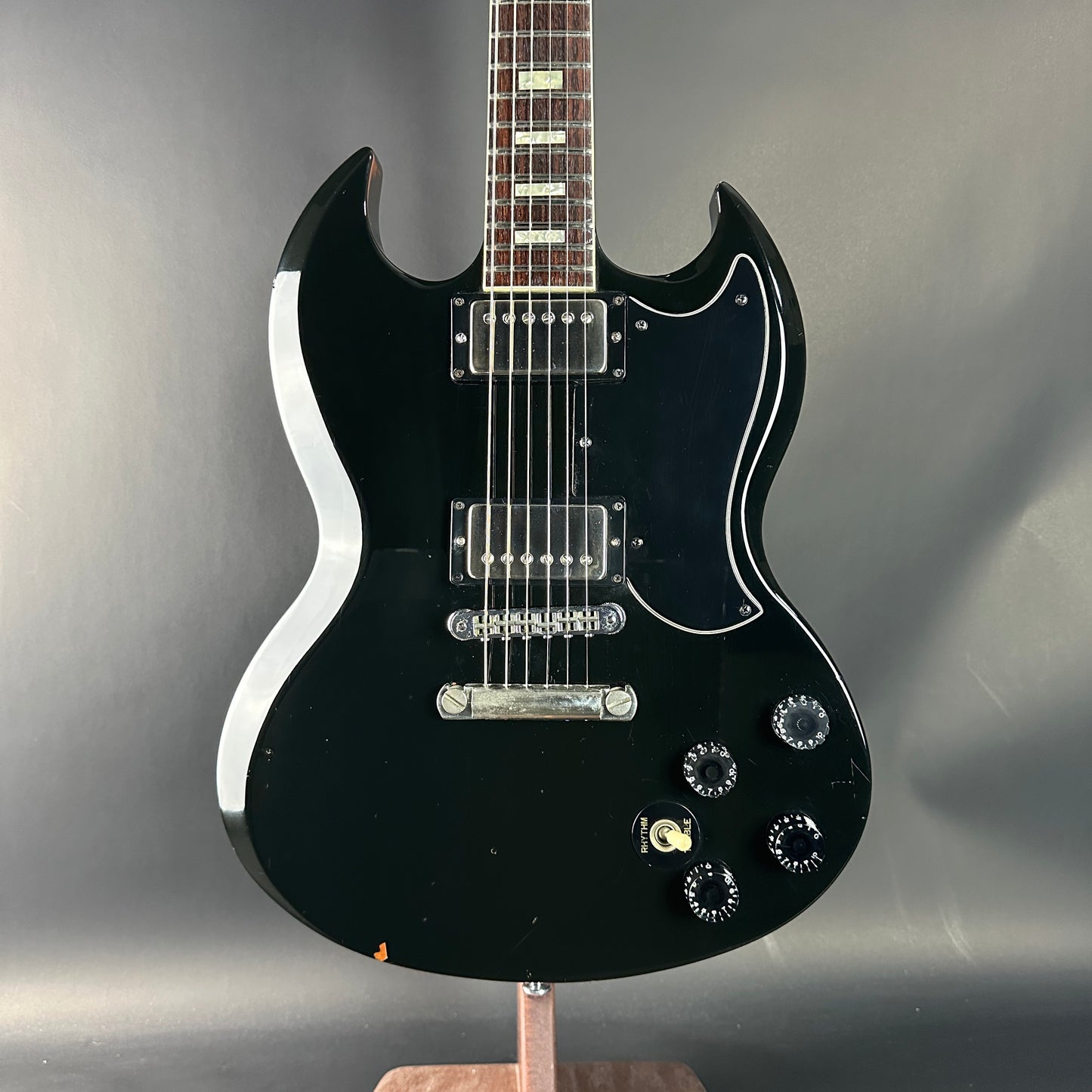 Black electric guitar on a stand against a gray background