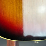 Close-up of a sunburst guitar body finish showing the transition from black to red and orange to amber, with a light wood edge and a small silver tuning peg visible.