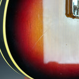 Close-up of a sunburst electric guitar body showing the red, orange, and black gradient finish, a white binding edge, and part of a chrome hardware component.