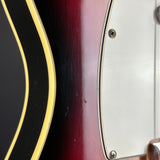 Close-up detail of an electric guitar body showing a dark red burst finish, a black section with gold binding, and a white pickguard with screws.