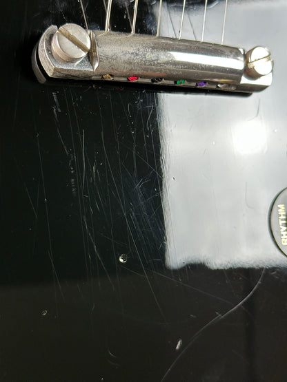 Close-up of a guitar's tuners on a black guitar body with visible wear.