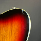 Close-up detail of an electric guitar body showing the sunburst finish transitioning from amber-orange to black, with a white binding edge against a dark gray background.