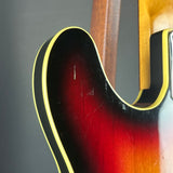 Close-up of a classic sunburst electric guitar body showing the red and amber gradient finish, black edge trim, and gold binding.