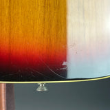 Close-up of a sunburst wood finish guitar body showing the transition from amber to red to black, with visible scratches on the glossy surface and a small metal tuning peg below.