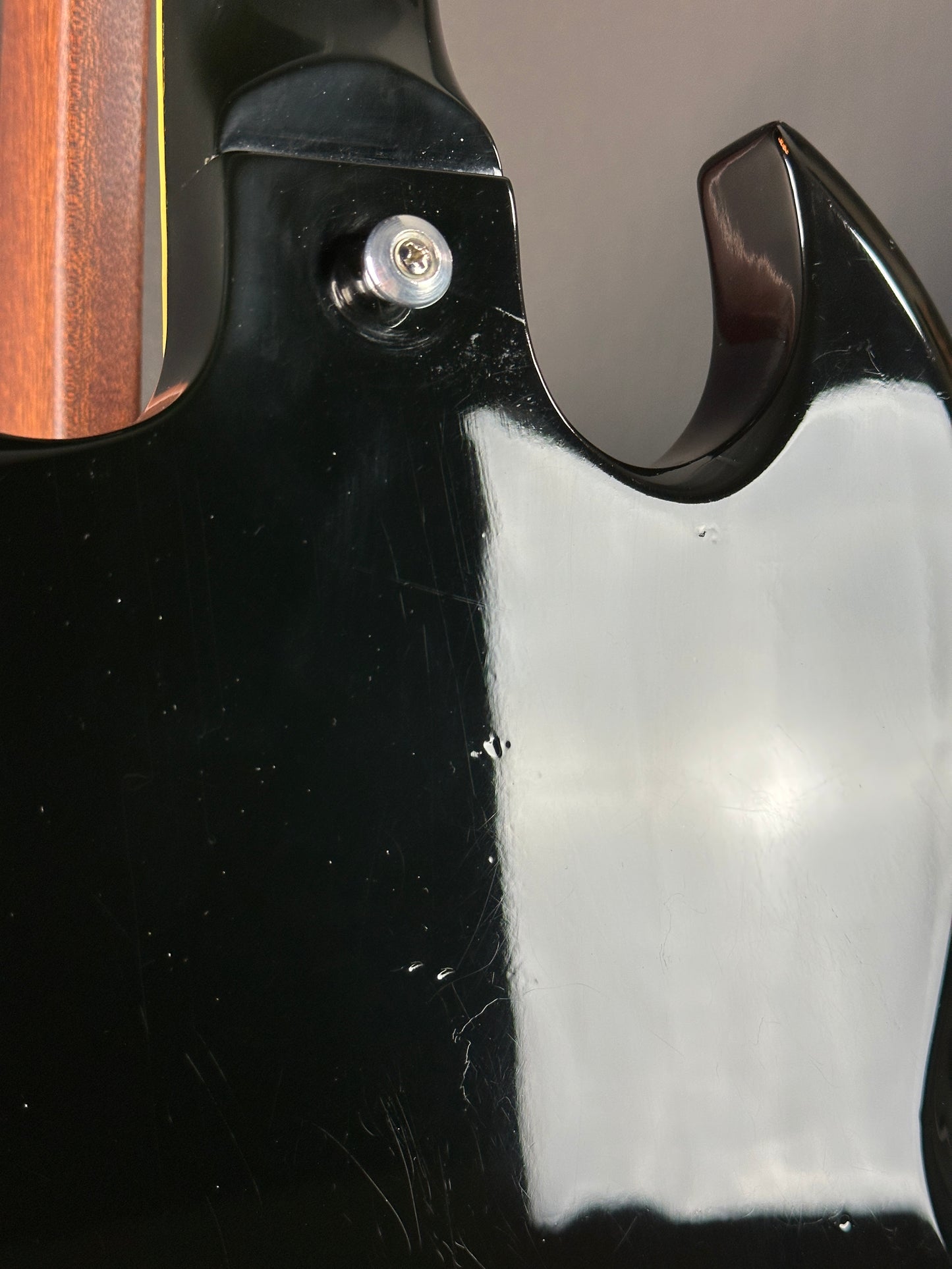 Close-up of a guitar's headstock with a screw and black finish.