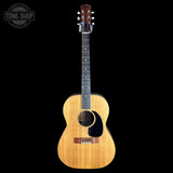 A classic acoustic guitar with a natural wood body, dark fretboard, and black pickguard, shown against a solid black background with a Tone Shop watermark in the top left corner.