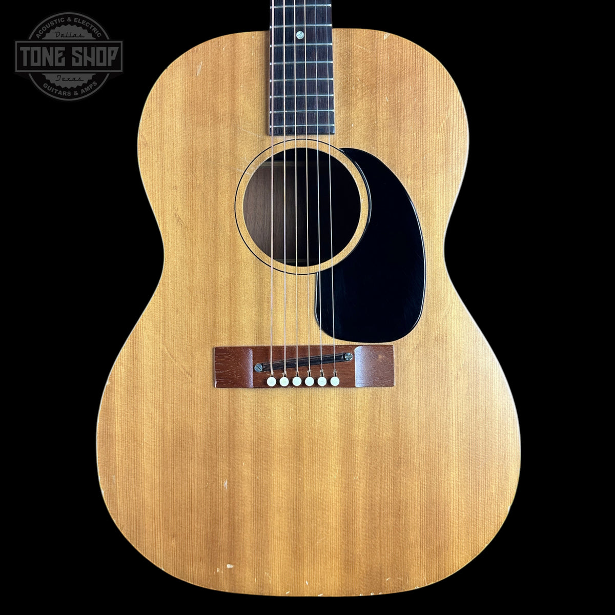 A vintage acoustic guitar with a natural wood body, black pickguard, and dark fretboard, shown against a solid black background. A 'TONE SHOP' watermark is visible in the top left corner.