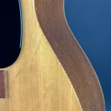 Close-up detail of a guitar body showing the natural wood grain, the dark pickguard, and a blue background.