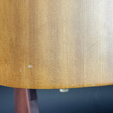 Close-up of a light brown wood grain surface with a few small scratches and a small piece of debris near the bottom edge, with a dark blue background visible below.