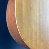 Close-up detail of a wooden object showing a light honey-toned wood grain surface and a darker reddish-brown curved edge against a dark blue background.
