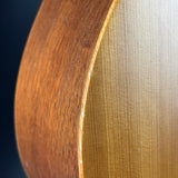 Close-up of a curved wooden surface showing two wood grain finishes: a darker reddish-brown on the left and a lighter honey-gold on the right, against a dark background.