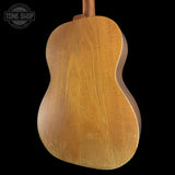The back of a wooden acoustic guitar, showing the natural wood grain and finish, photographed against a solid black background with a Tone Shop watermark in the top left corner.