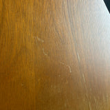 A close-up of a brown wood-grain surface with visible scratches and scuffs.