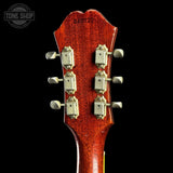 Close-up of a guitar headstock with tuning pegs on a black background, featuring 'Tone Shop' branding.