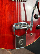 Close-up of a guitar's bridge and tuning pegs on a red guitar body.