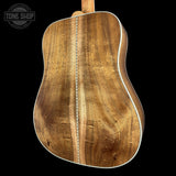 Close-up of the back of an acoustic guitar showing the natural wood backplate grain, white edge trim, and a vertical center seam, photographed against a black background with a Tone Shop watermark in the upper left.