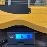 A close-up of a yellow electric guitar body resting on a black digital smart scale displaying 6.78 kg, with the guitar's black pickguard and part of the headstock visible.