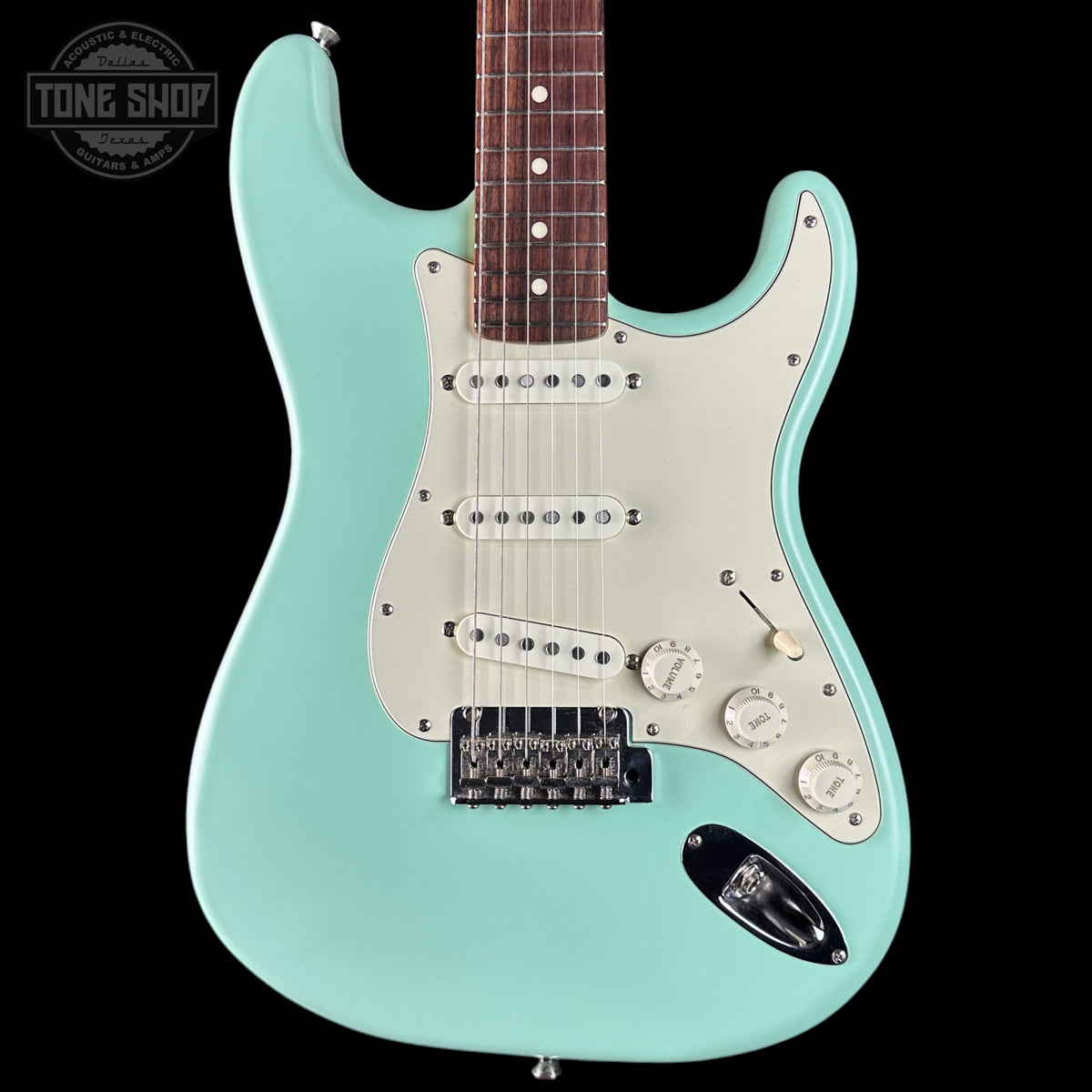 Turquoise electric guitar with a white pickguard on a black background, featuring the Tone Shop logo.