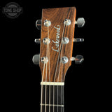 Close-up of the headstock of a Lakewood acoustic guitar, showing the dark brown wood grain, six silver tuning pegs, and six strings against a solid black background.