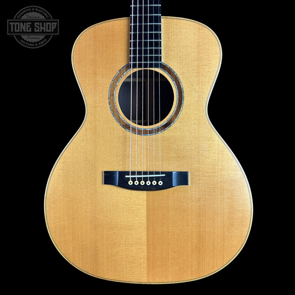 A front-facing acoustic guitar with a natural wood finish and black hardware, shown against a solid black background with a Tone Shop logo in the top-left corner.