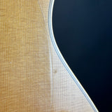 Close-up detail of an acoustic guitar body showing the natural wood grain top, the white edge trim, and a dark navy blue soundhole surround.