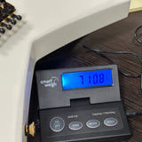 A close-up of a smart weigh digital scale displaying '710.8 kg' on its blue backlit screen, resting on a dark wooden surface next to a white machine body.