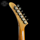 Close-up of the headstock of a Fender Stratocaster electric guitar in a glossy natural wood finish, featuring six silver tuners and a black Fender logo, set against a solid black background.