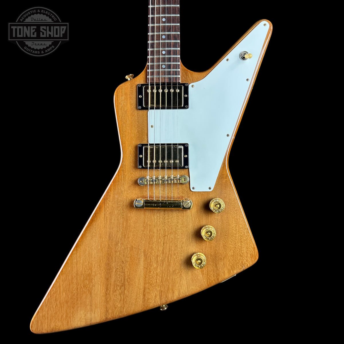 A classic electric guitar with a natural wood finish, a white pickguard, and gold hardware, shown against a solid black background with a Tone Shop watermark in the top left corner.