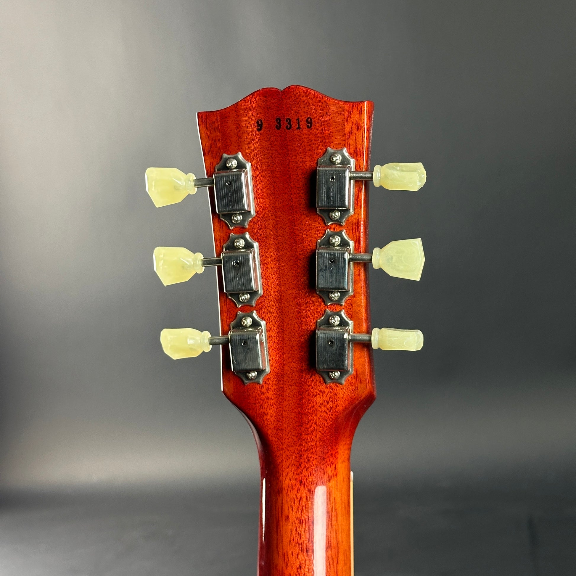 Close-up of a guitar headstock with tuning pegs on a gray background