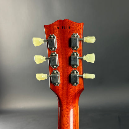 Close-up of a guitar headstock with tuning pegs on a gray background
