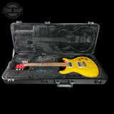 A yellow electric guitar with a red headstock resting inside an open black hard case with black foam lining, shown against a black background. A Tone Shop watermark is visible in the top-left corner.