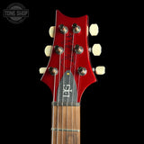 Close-up of a red electric guitar headstock with six cream tuning pegs, a black pickguard, and a dark fretboard, shown against a black background with a Tone Shop watermark in the top left.