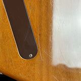 Close-up of a wooden guitar body with a dark brown pickguard and visible surface scratches and wear.