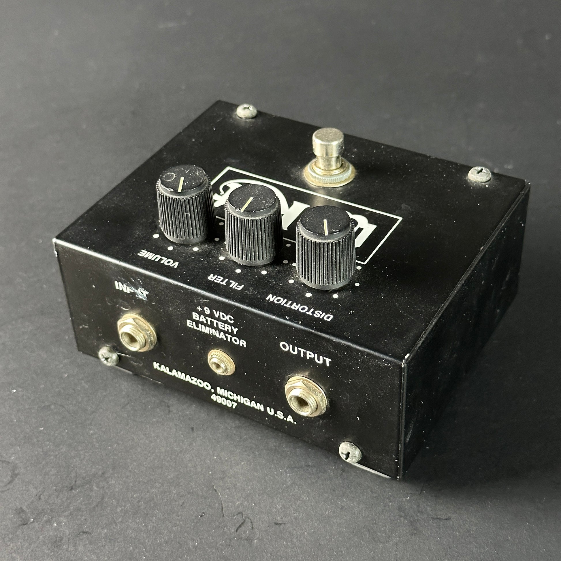 Black guitar effects pedal with knobs and labels on a dark gray background