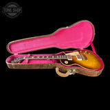 An electric guitar with a sunburst finish displayed inside an open hard case with a bright pink velvet interior, set against a solid black background with a Tone Shop watermark in the top left corner.