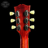 Close-up of the headstock of an acoustic guitar, showing six cream-colored tuning pegs and black tuning machines on a glossy red wood finish, set against a solid black background.