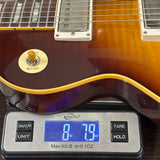 A close-up of a guitar body resting on a digital scale, showing the instrument's sunburst finish, pickguard, and part of the neck. The scale reads 8 lbs 7.