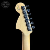 Close-up of the headstock of a Fender electric guitar in natural wood finish with black tuning pegs, shown against a solid black background. A Tone Shop watermark is visible in the top left corner.